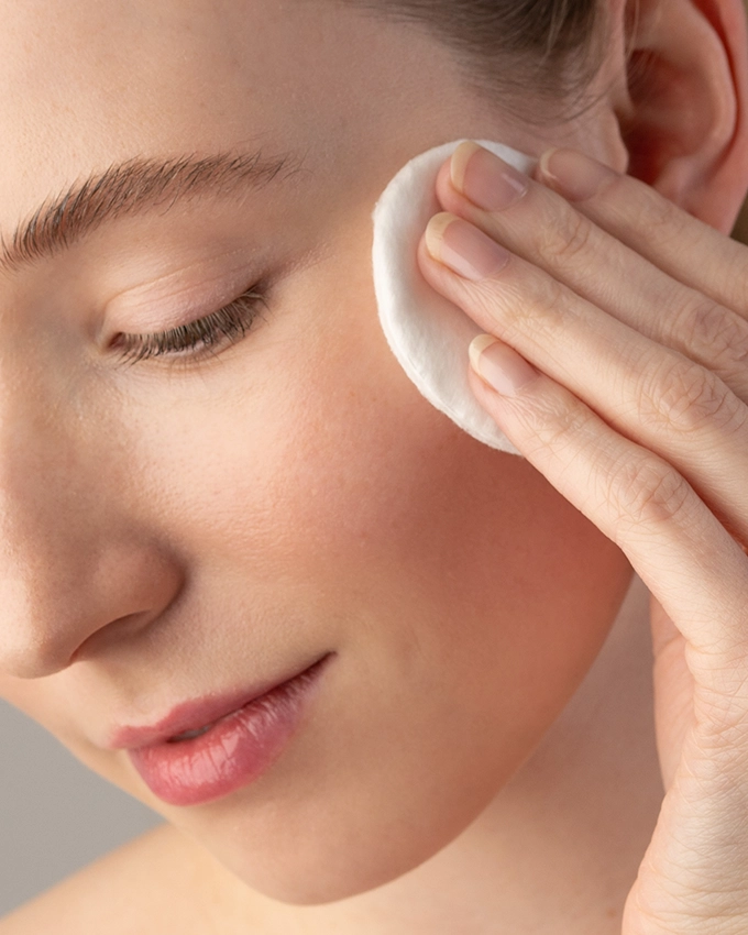 Woman cleanses face with cotton pad and tonic