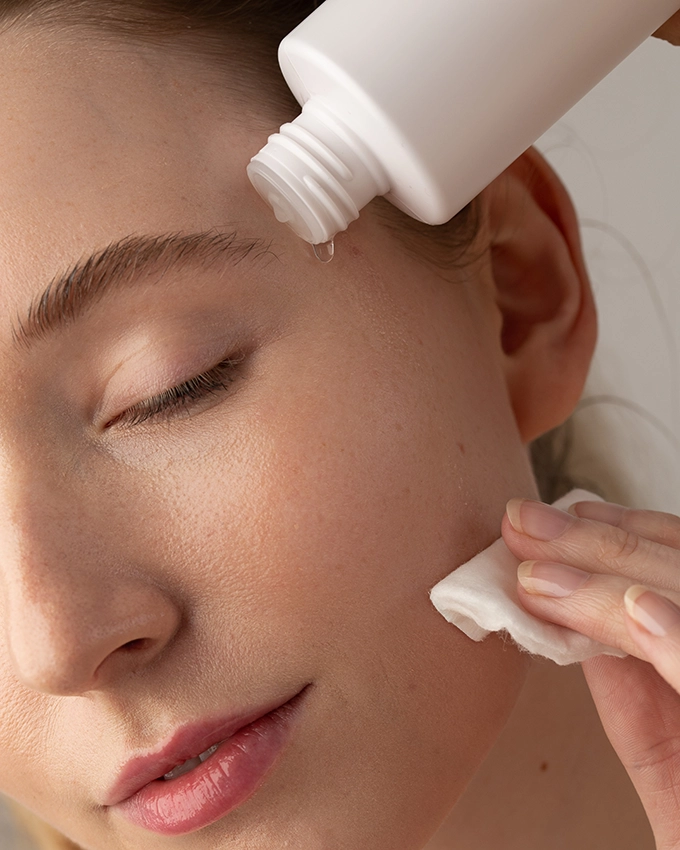 Woman cleanses face with cotton pad and tonic