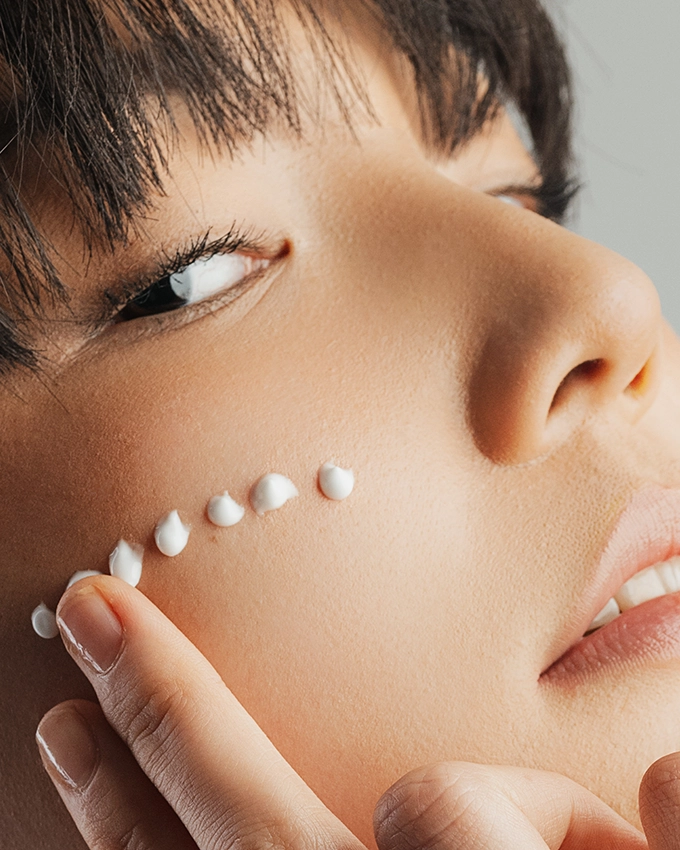 Serum wird punktuell auf Wange von Frau aufgetragen