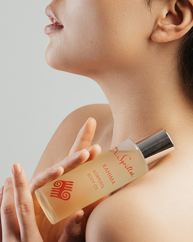 Rahima body oil is held in front of woman's shoul