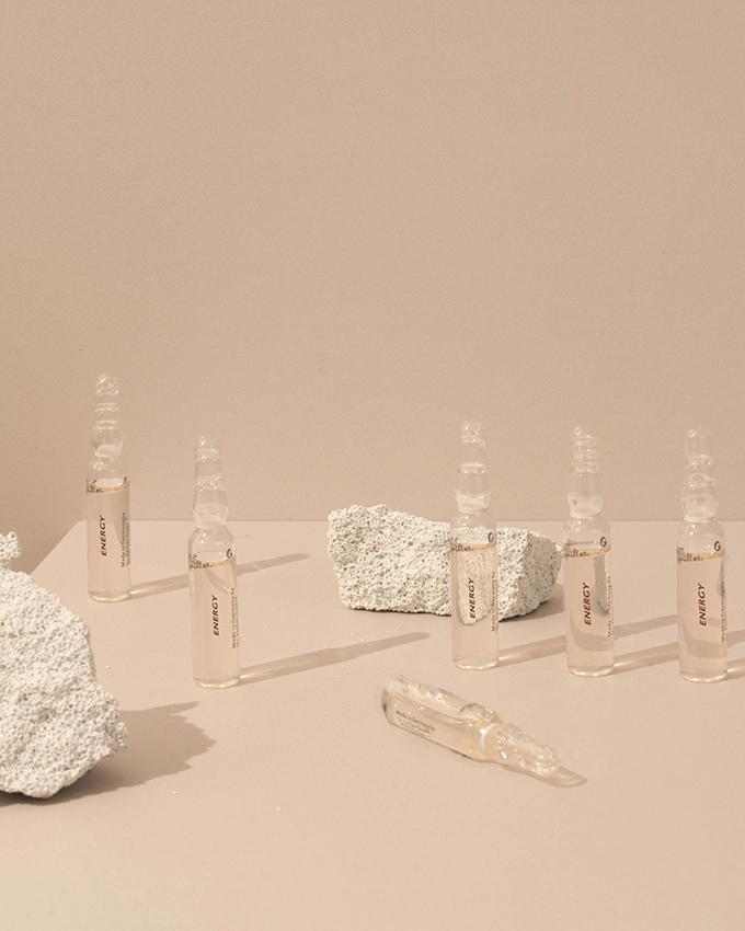 Several ampoules are placed on a table with a pink background