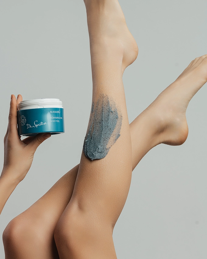 Manaru body scrub is held in the air and applied to woman's leg