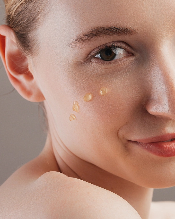 Serum wird punktuell auf Wange von Frau aufgetragen