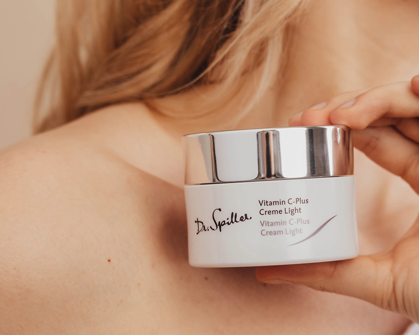 Woman holding Vitamin C Plus Creme Light jar in front of her collarbone