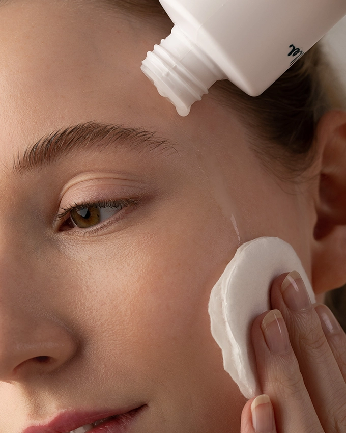 Frau reinigt Gesicht mit Wattepad und Tonic