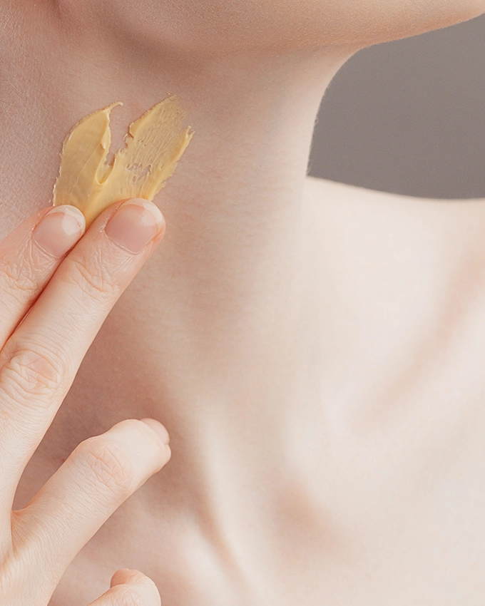 Gebliche Creme wird auf Hals mit Fingern aufgetragen